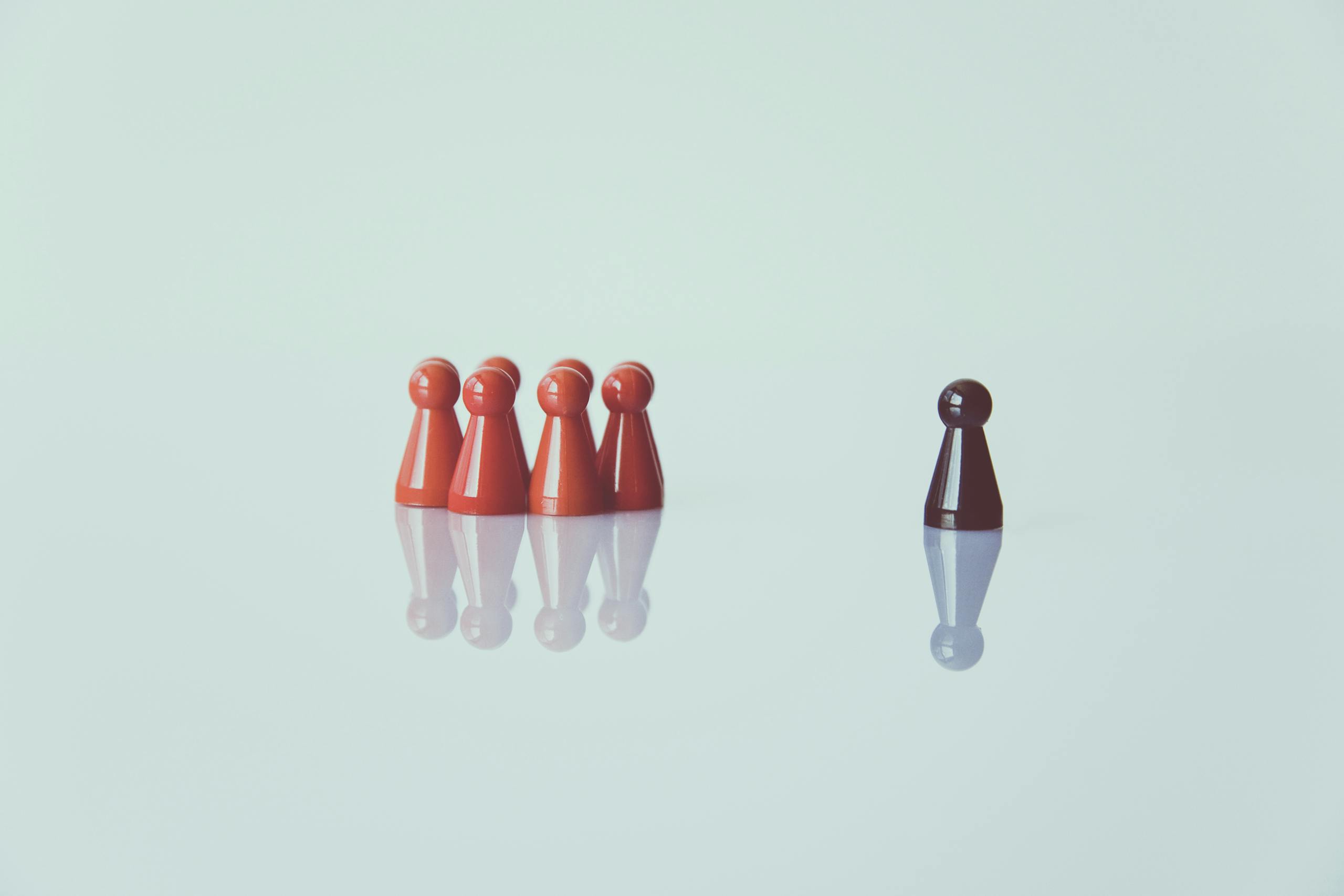 Red game pieces grouped with one isolated piece symbolizing social distancing on a reflective surface.